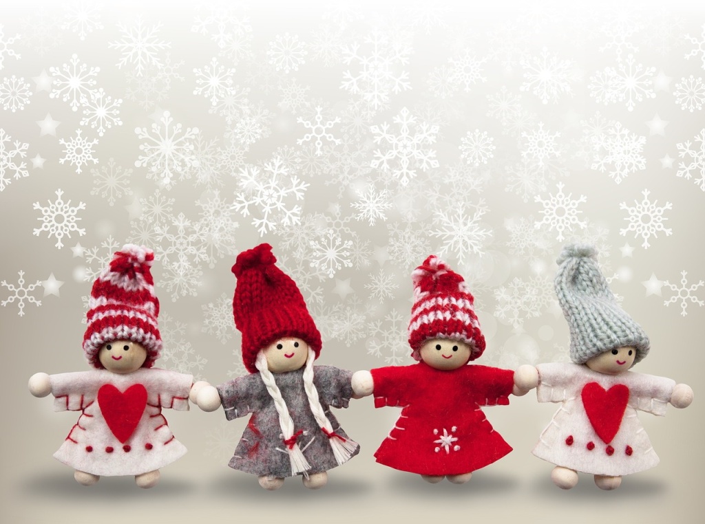 Four little wooden dolls in Christmas outfits, against a background of falling snowflakes